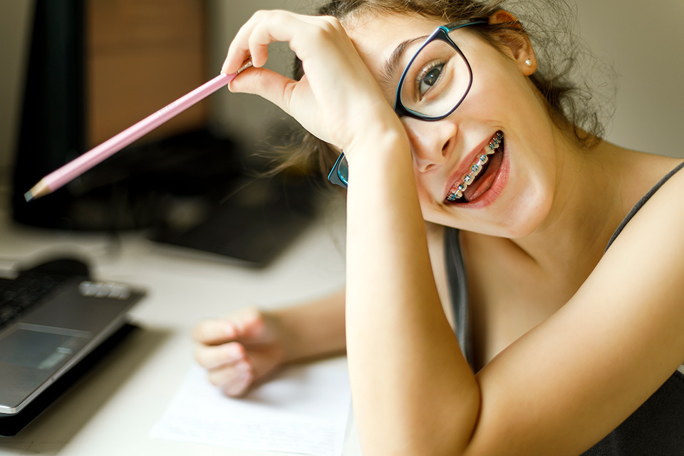 a child with braces holding a pencil and smiling for the camera